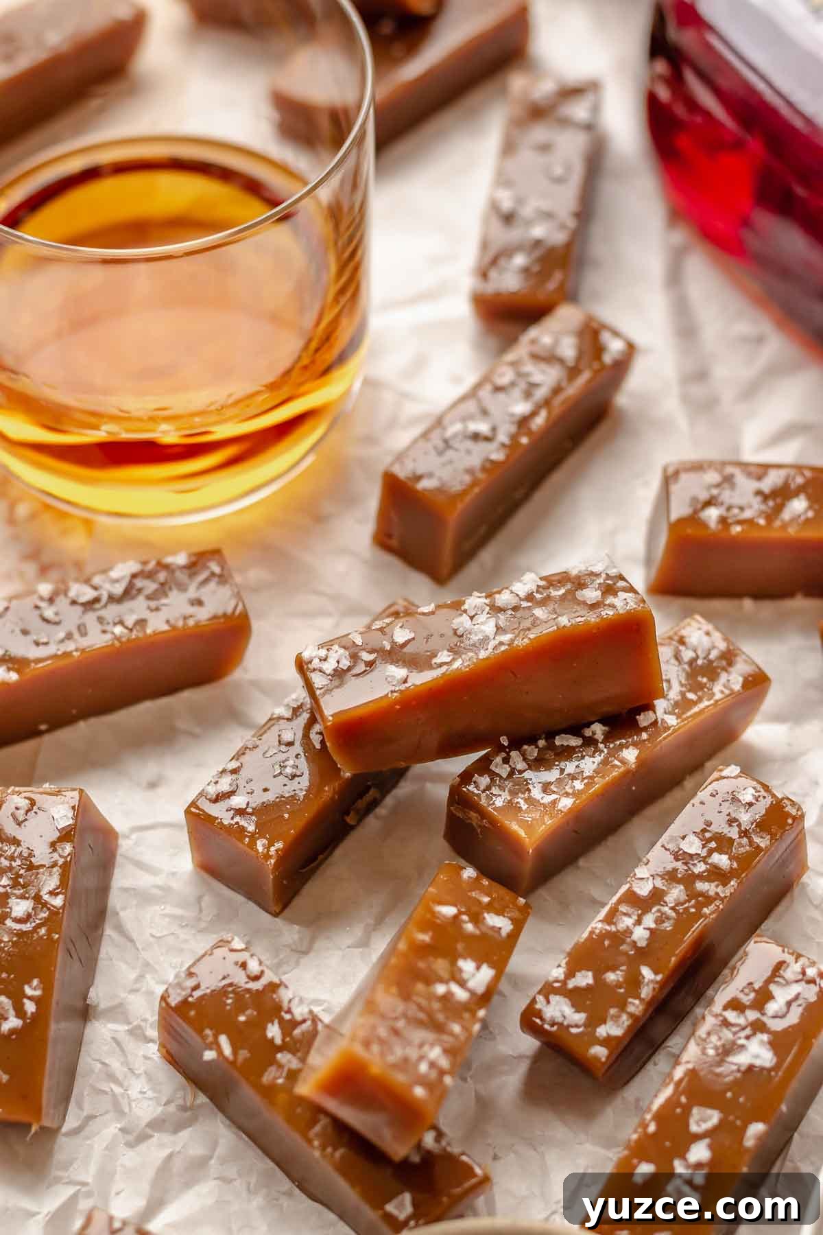 Salted Bourbon Caramel Candies: Sticky Sweet Whiskey Caramels 12 Salted whiskey caramels laid about with a glass of whiskey in the back.