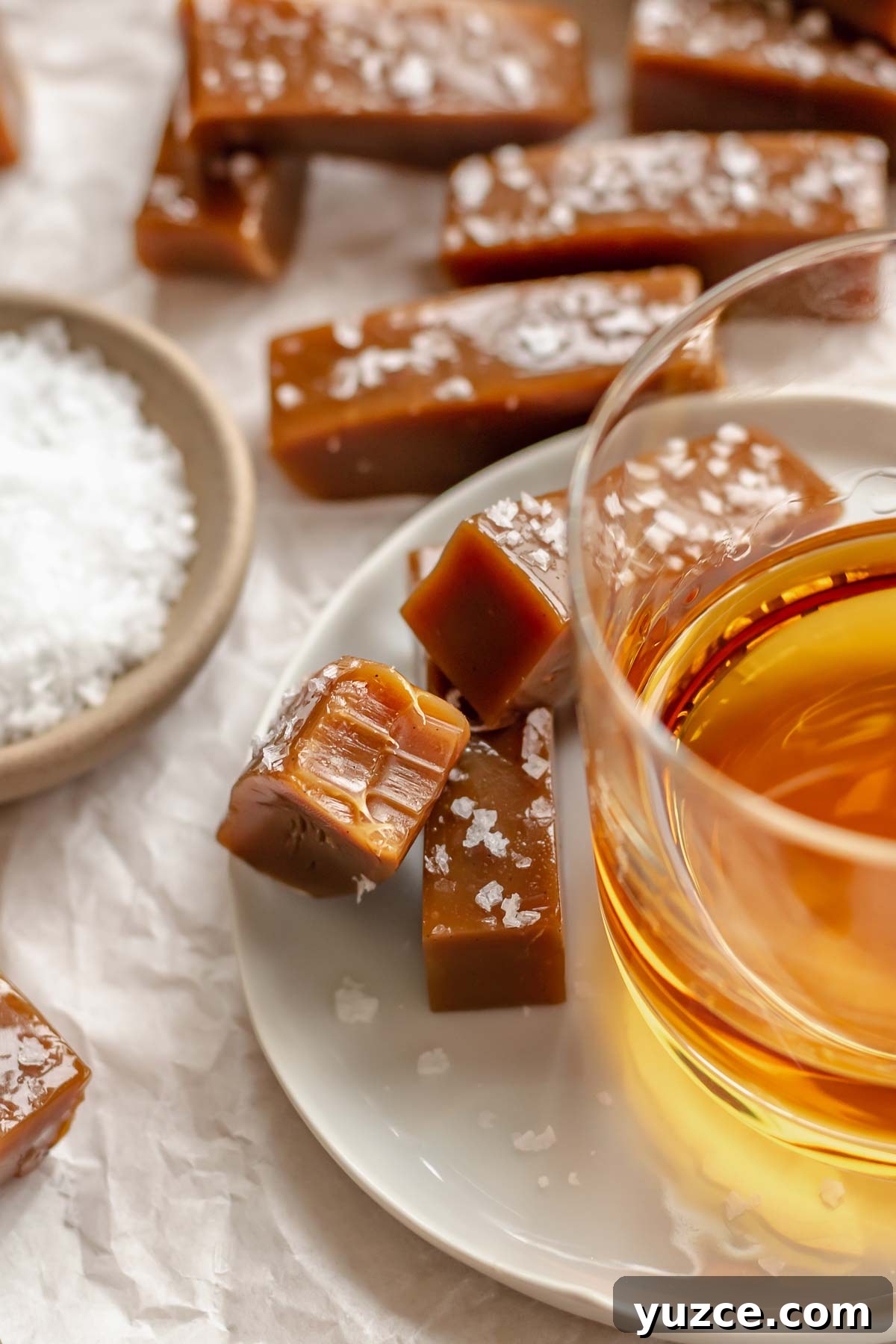 Salted Bourbon Caramel Candies: Sticky Sweet Whiskey Caramels 13 Salted caramels on a plate next to a glass of whiskey.