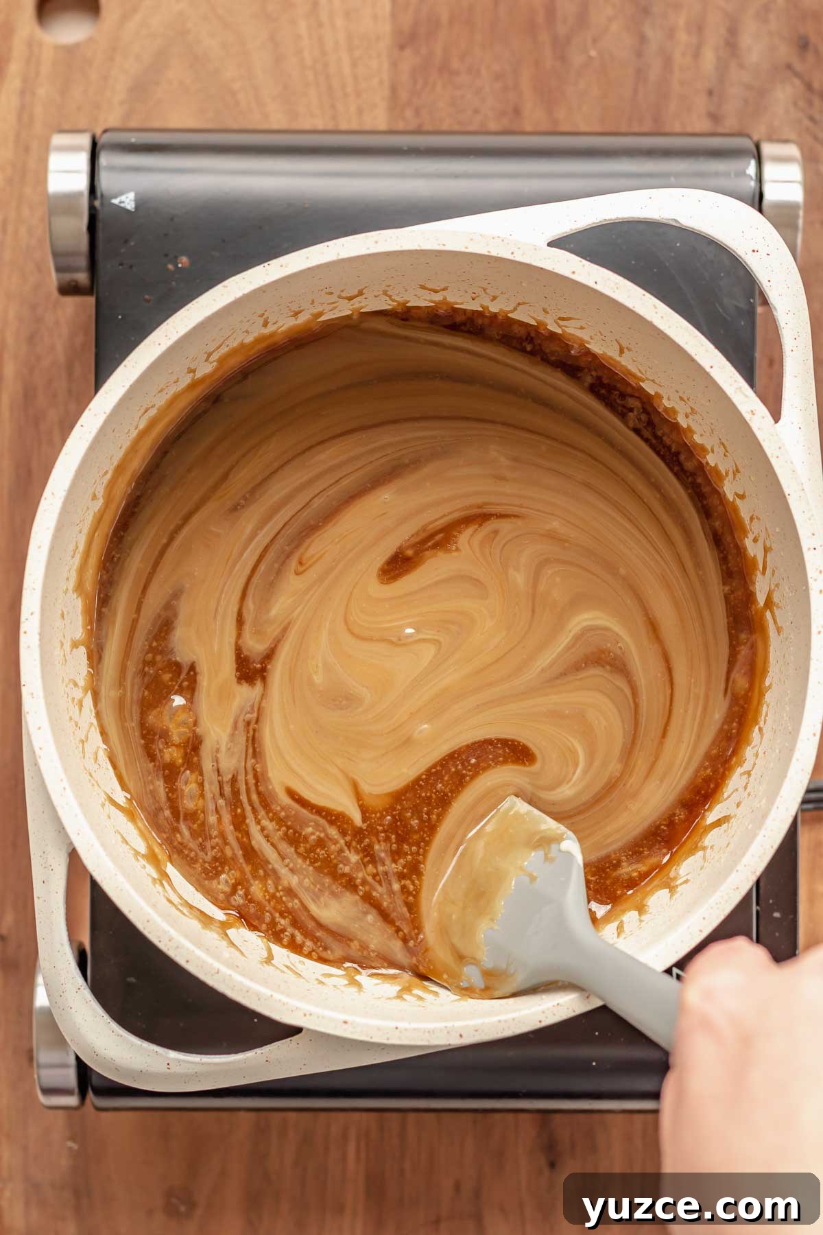 Salted Bourbon Caramel Candies: Sticky Sweet Whiskey Caramels 7 A spatula stirs sweetened condensed milk into a pot.