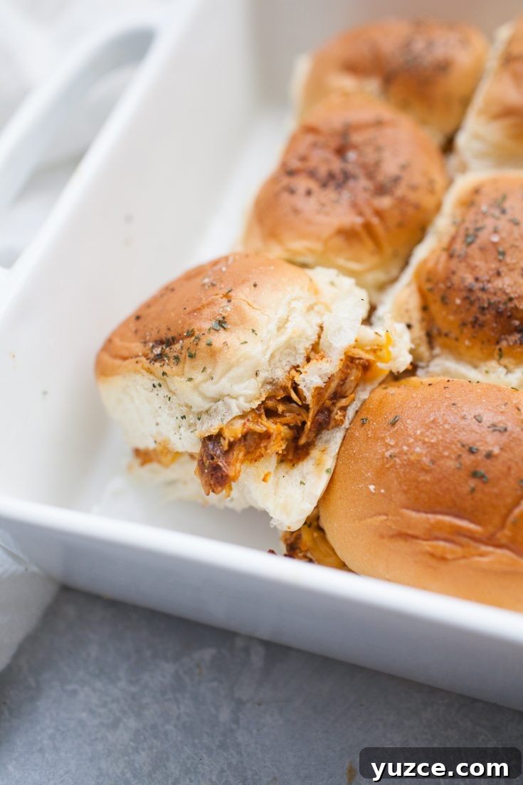 Sweet Pepper Jelly and Cream Cheese Dip Recipe for Entertaining 12 A tray of six cooked, evenly browned chicken sliders filled with shredded meat, topped with seasoning. One slider is slightly pulled apart from the rest, revealing the flavorful interior filling.
