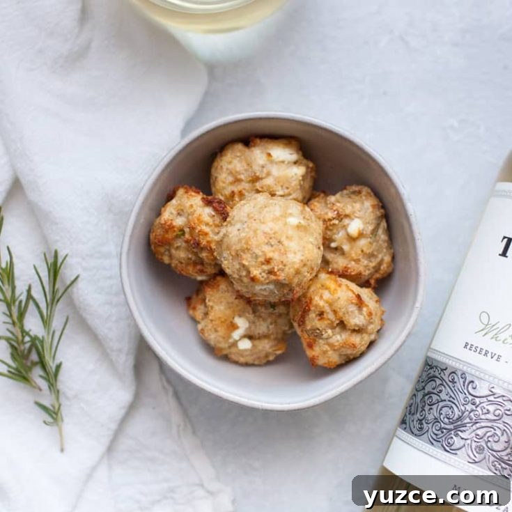 Sweet Pepper Jelly and Cream Cheese Dip Recipe for Entertaining 13 A bowl of baked chicken meatballs beside a bottle of white wine on a white surface, adorned with a sprig of rosemary and a white linen cloth.