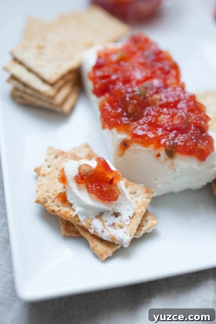 Sweet Pepper Jelly and Cream Cheese Dip Recipe for Entertaining 7 A white plate with crackers, cream cheese, and a vibrant layer of pepper jelly spread on top.