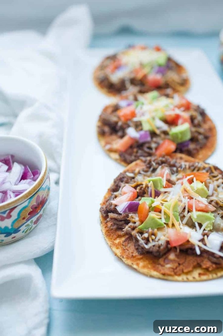 Sweet Pepper Jelly and Cream Cheese Dip Recipe for Entertaining 10 A white rectangular plate with three Mexican tostadas topped with shredded meat, diced tomatoes, avocado, shredded cheese, and onions. A small bowl of diced red onions is on the side.
