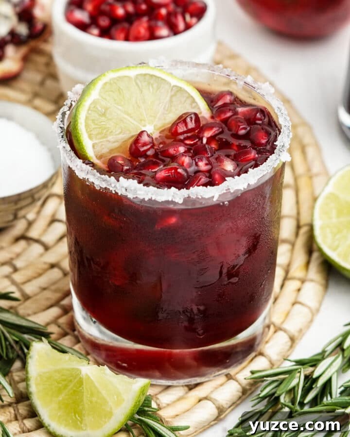 Pomegranate margarita on a wicker placemat with fresh lime and rosemary.