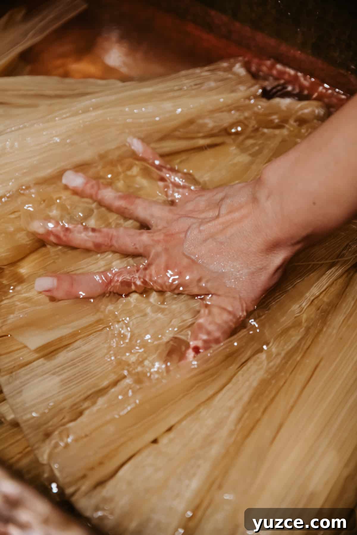 How to Host a Tamalada: Step-by-Step Tamal-Making Party Guide 6 woman's hand pressing corn husks into cool water to soak before hosting a tamale-making party.