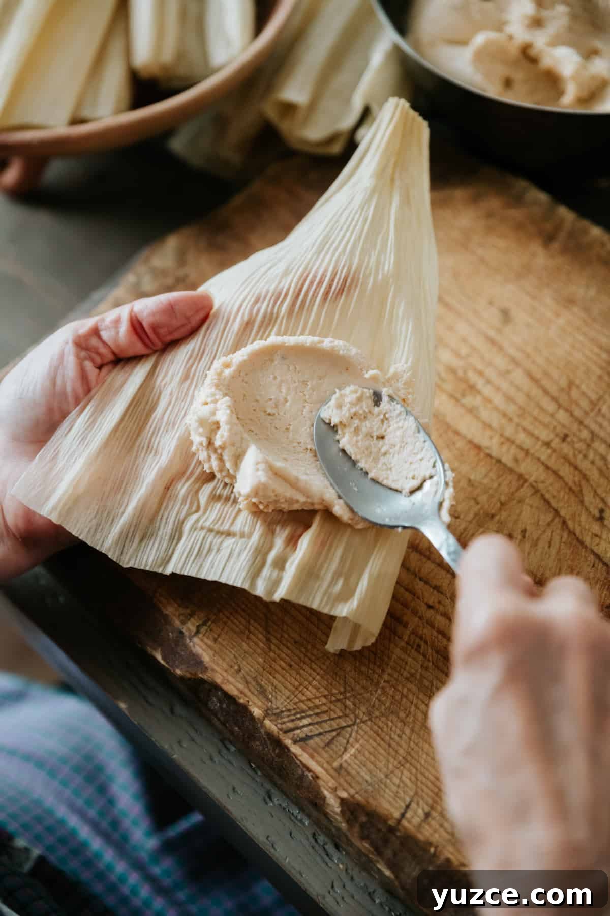How to Host a Tamalada: Step-by-Step Tamal-Making Party Guide 7 using a spoon to spread masa dough on a corn husk for a tamal.
