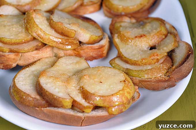 Maple Pear Crostini: Quick Fall Appetizer with Warm Flavor 9 Oblique close up of a batch of maple pear crostini on a white ceramic platter sitting on a green wooden table | Foodal