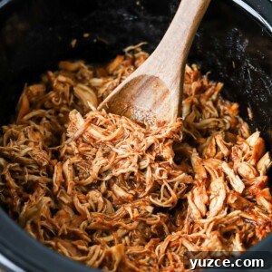 Brown sugar BBQ chicken in a slow cooker with a wooden spoon.
