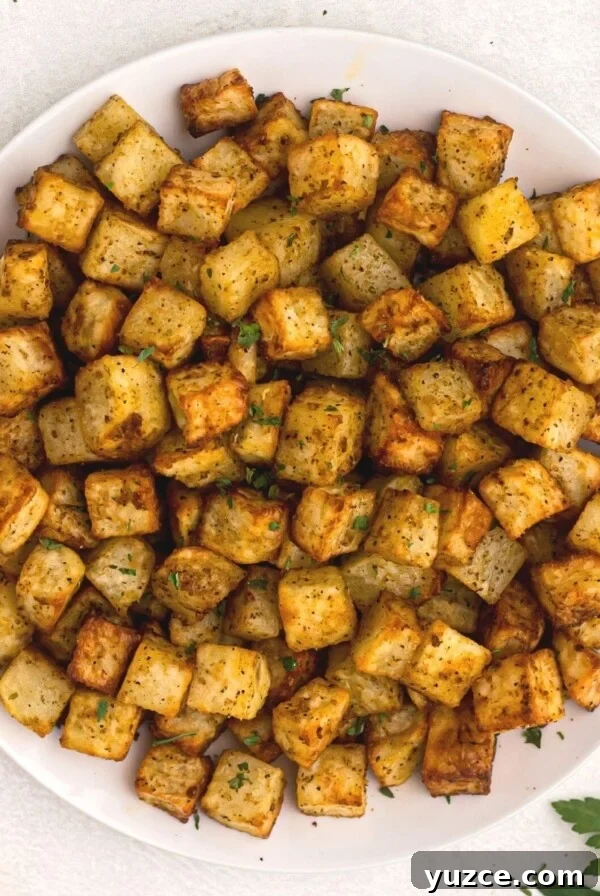 Crispy Air Fryer Home Fries Recipe for Breakfast or Brunch 13 Golden cubes of potatoes cut and cooked served on a white plate and garnished with parsley.