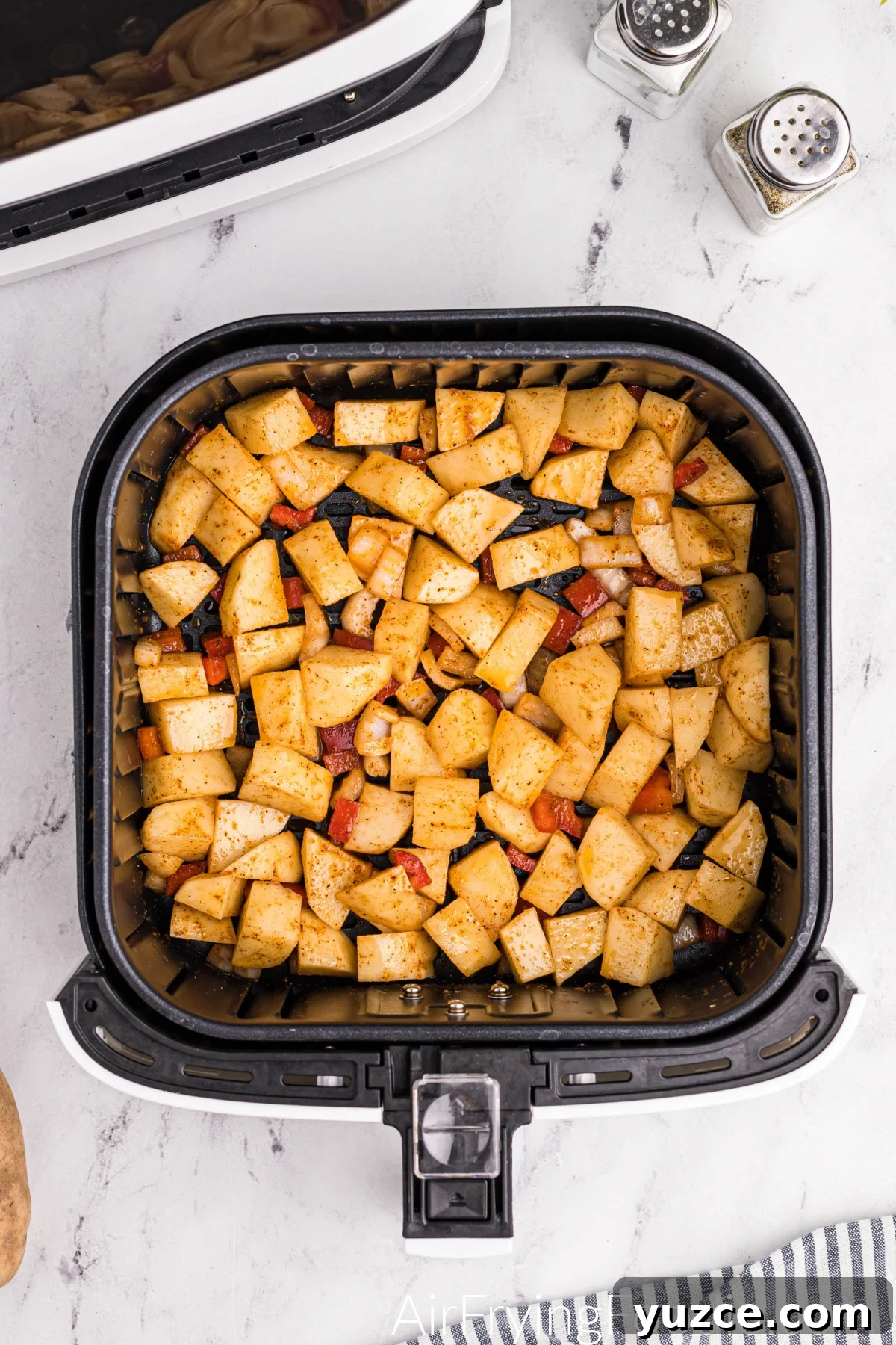 Crispy Air Fryer Home Fries Recipe for Breakfast or Brunch 7 Diced potatoes seasoned and mixed with bell pepper and onion in the basket of the air fryer, ready to be cooked.
