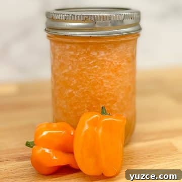 Pineapple habanero sauce in a glass jar with two habaneros on a butcher block counter.