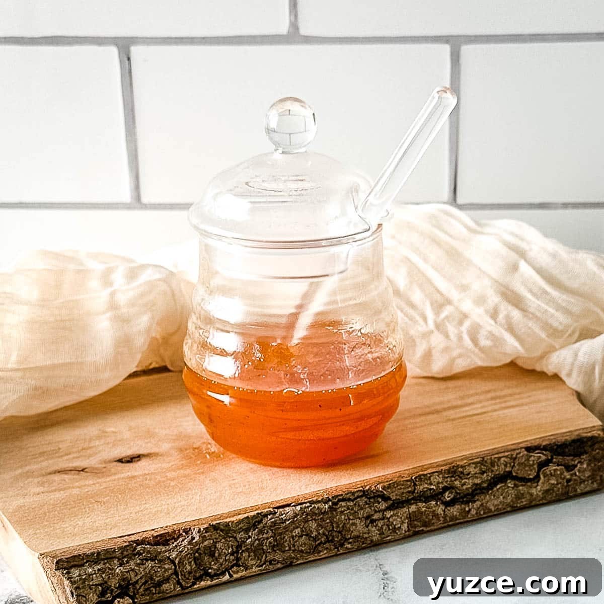 Homemade Hot Honey Sauce Recipe for Spicy-Sweet Dishes 7 Hot honey sauce in a glass jar on a rustic wooden cutting board with a white linen.