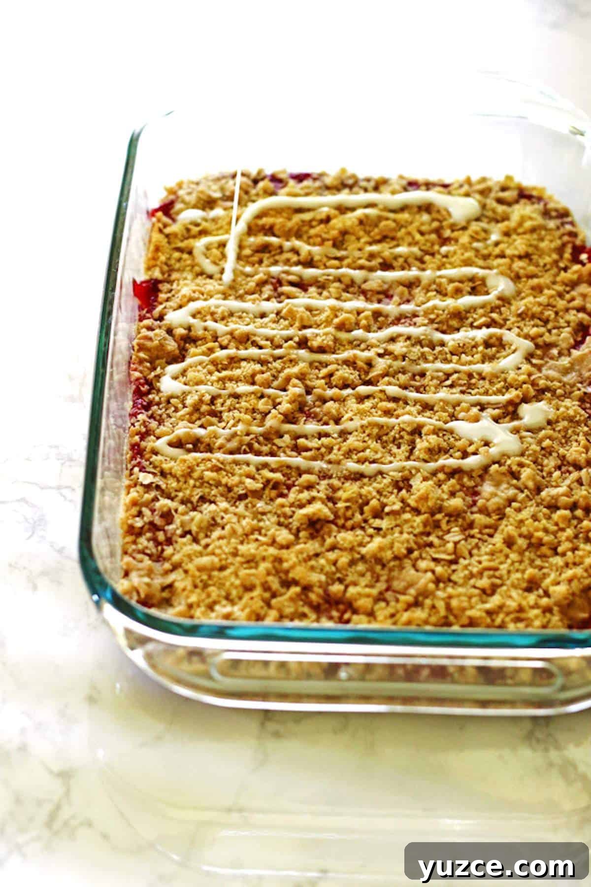 Strawberry Rhubarb Crumble Bars Recipe — Sweet Tart Dessert Bars 7 A pan of strawberry rhubarb bars with crumble topping and a sweet glaze on top.