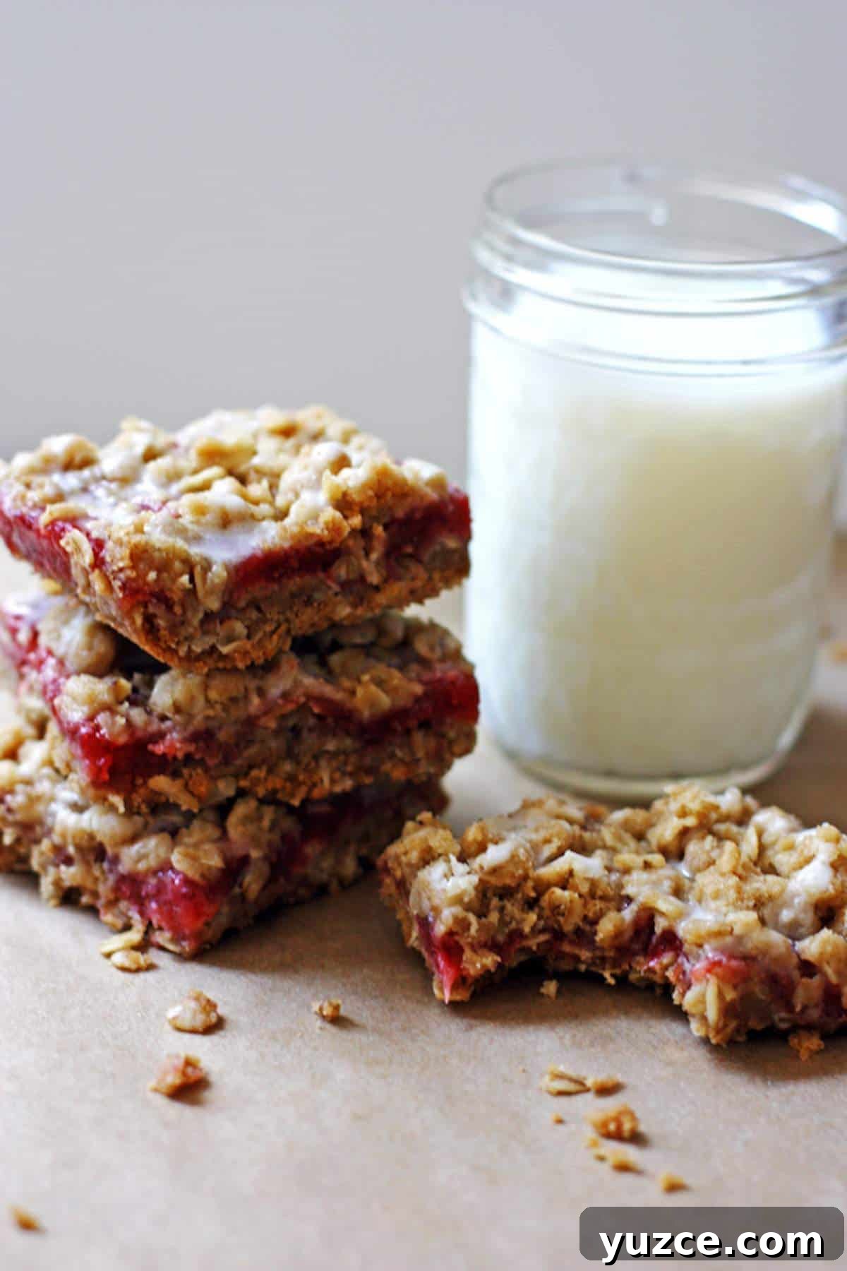 Strawberry Rhubarb Crumble Bars Recipe — Sweet Tart Dessert Bars 9 A pile of strawberry rhubarb bars with a glass of milk.