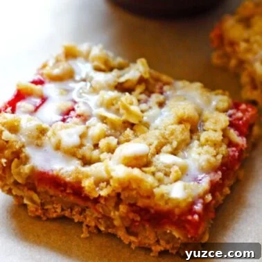 Strawberry Rhubarb Crumble Bars Recipe — Sweet Tart Dessert Bars 10 A glazed strawberry rhubarb crumble bar on a tray covered in brown parchment paper.