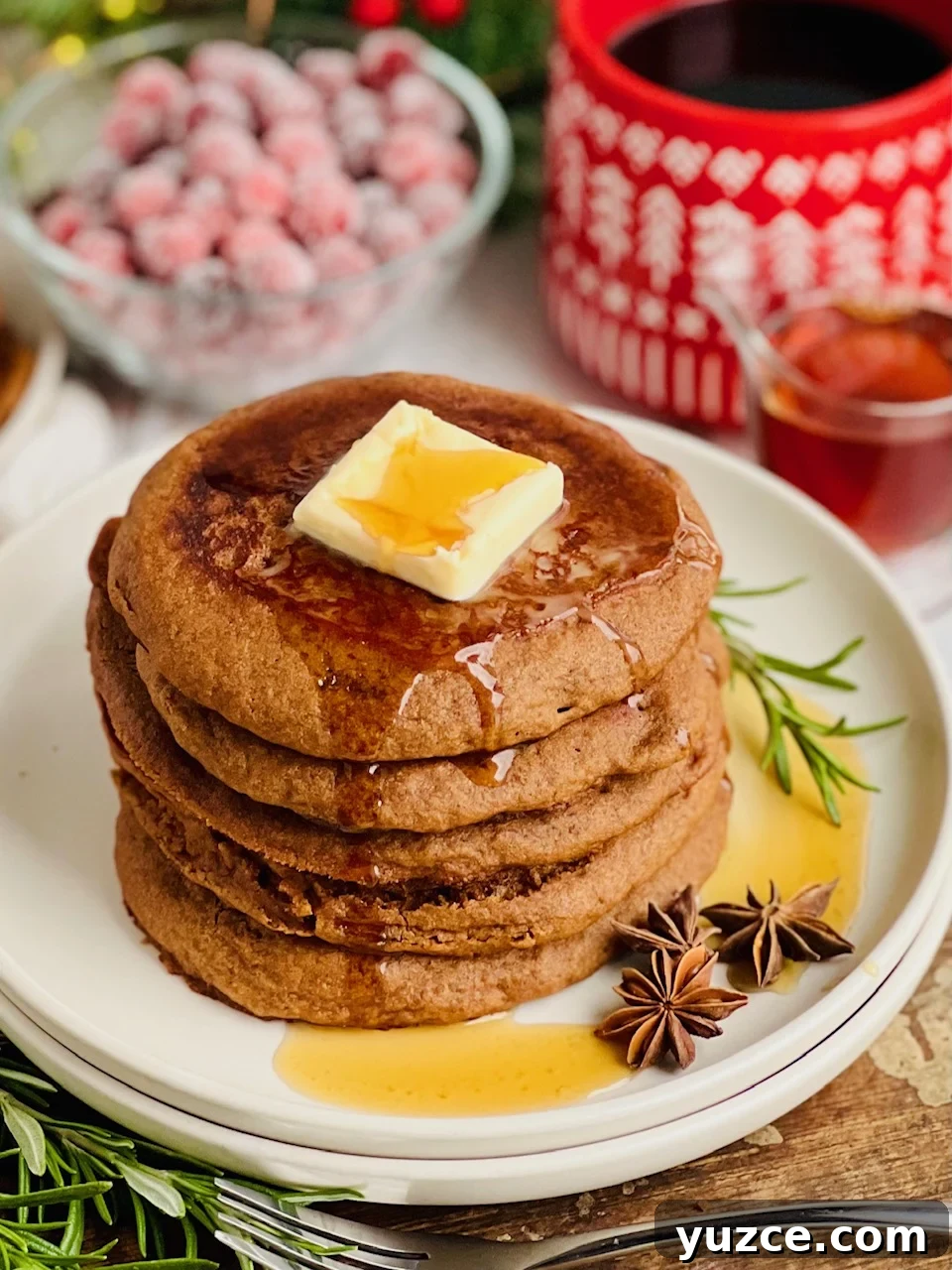 Gingerbread Pancakes with Warm Molasses Syrup 5 A white plate filled with dark brown colored round pancakes with a large square of melty butter and syrup running down the top.