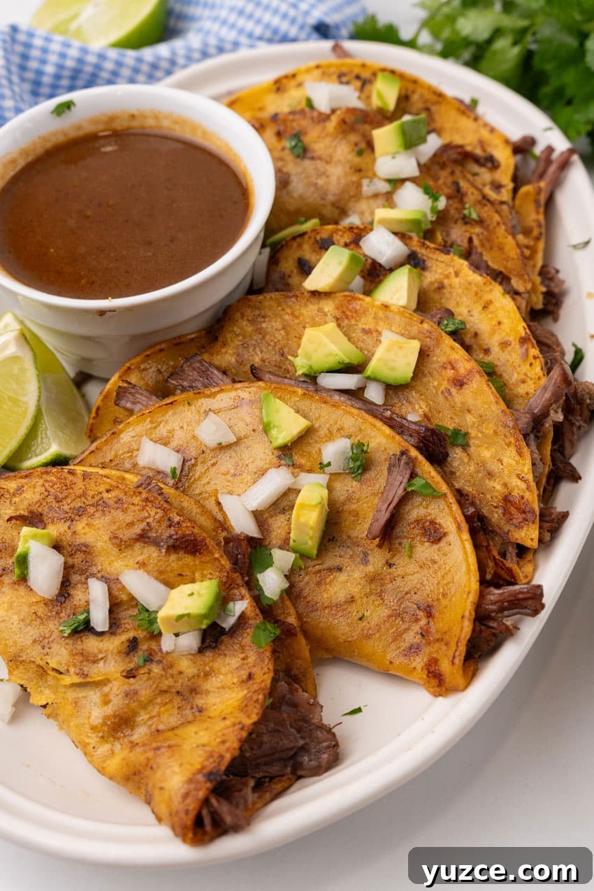 Instant Pot Birria Tacos Recipe: Flavorful Homemade Birria 2 instant pot birria tacos topped with avocado pieces and diced white onion arranged in a row on a white serving platter
