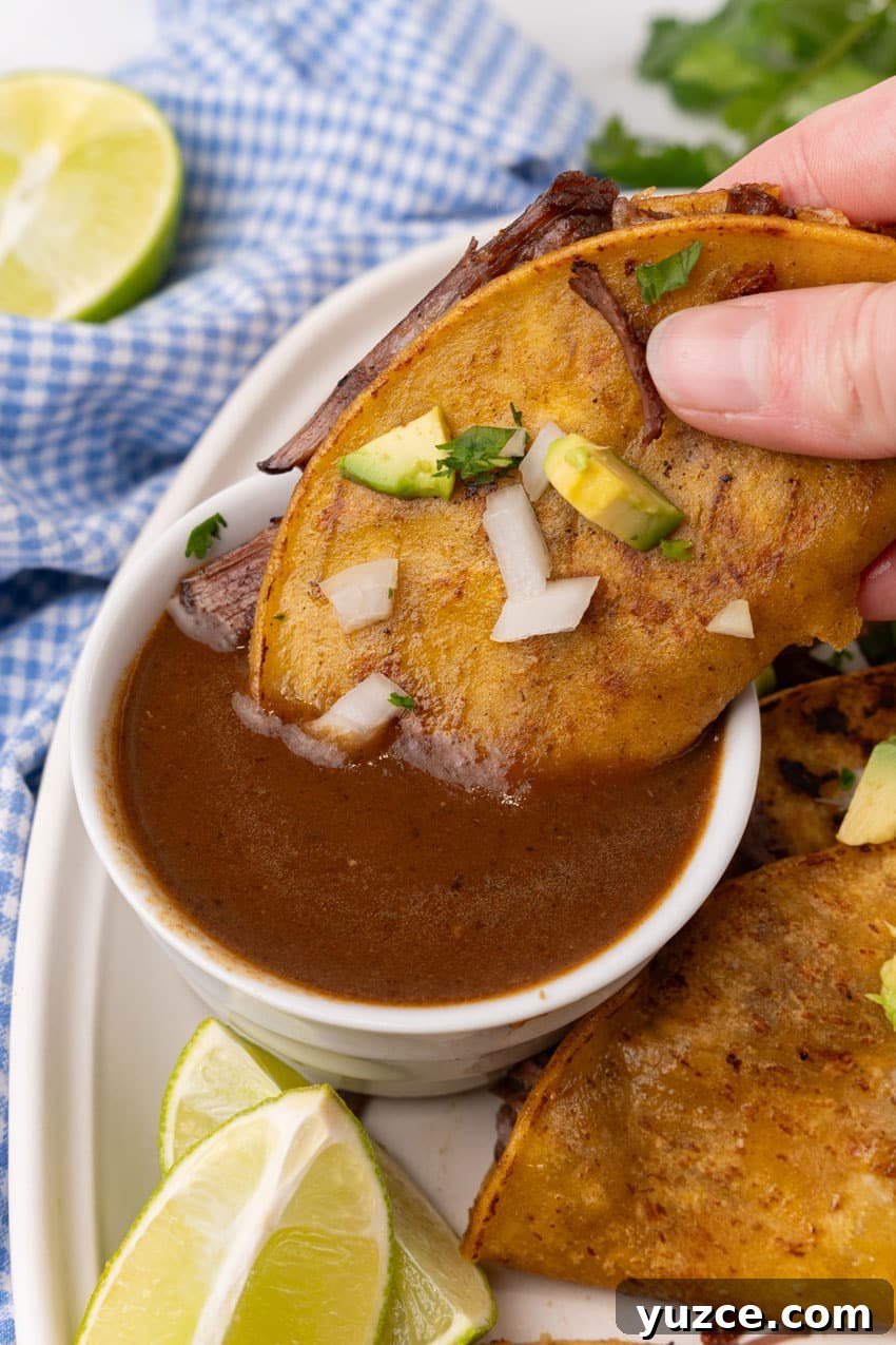 Instant Pot Birria Tacos Recipe: Flavorful Homemade Birria 11 a hand dipping a quesa birria taco in a small white bowl of birria sauce