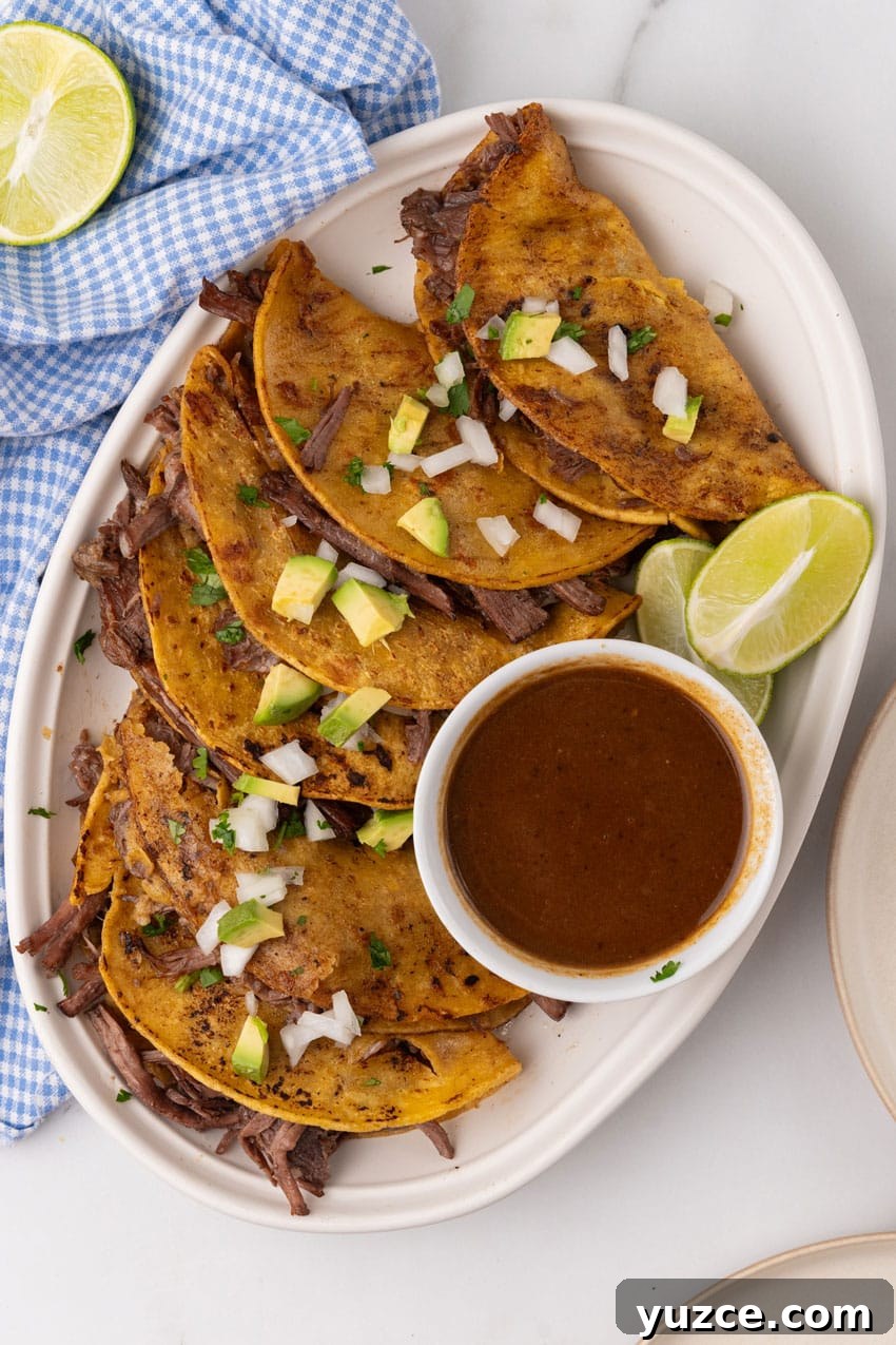 Instant Pot Birria Tacos Recipe: Flavorful Homemade Birria 3 instant pot birria tacos topped with avocado pieces and diced white onion arranged in a row on a white serving platter