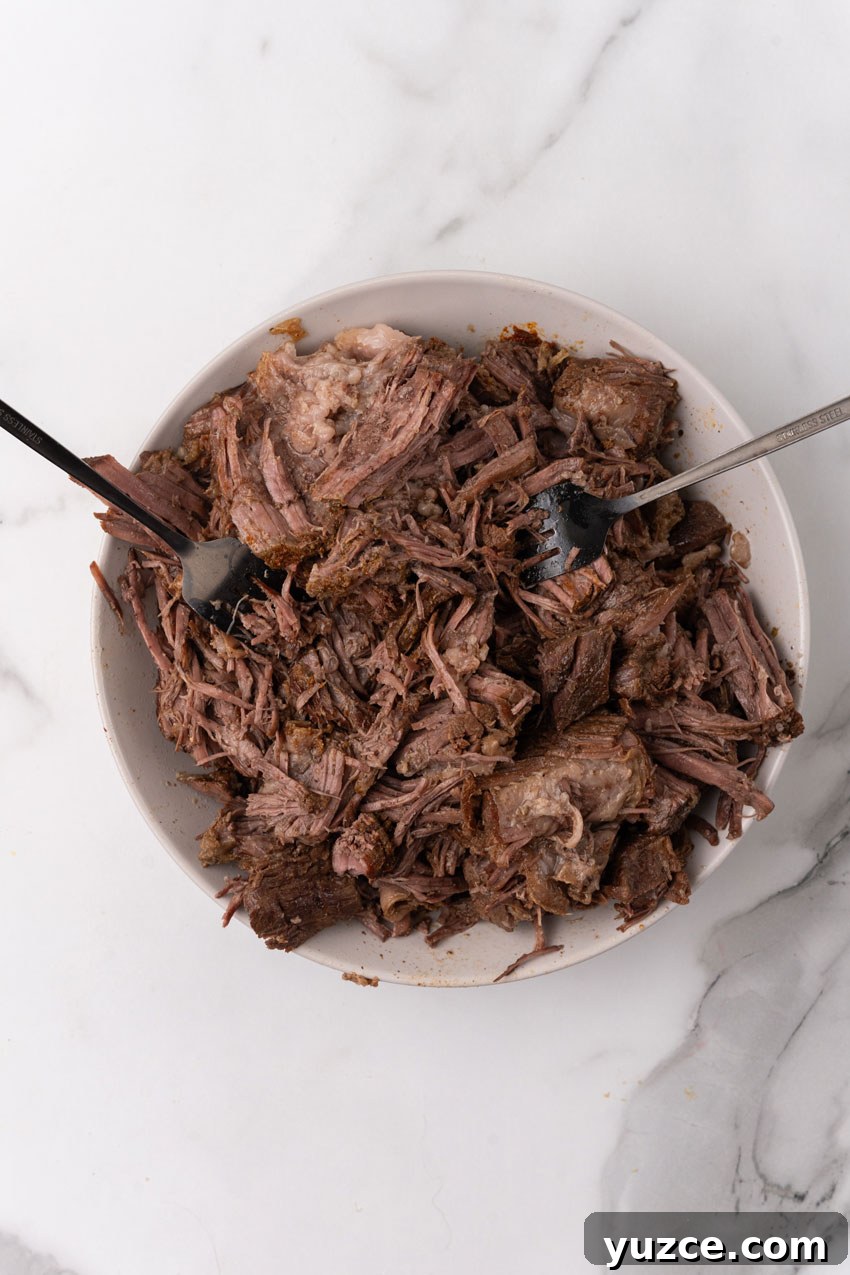 Instant Pot Birria Tacos Recipe: Flavorful Homemade Birria 8 shredded beef on a white plate with two forks resting on the side