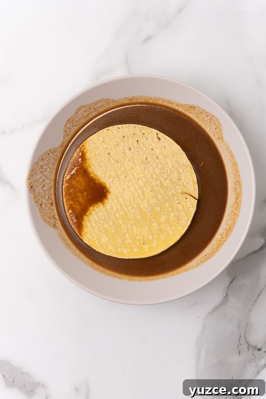 Instant Pot Birria Tacos Recipe: Flavorful Homemade Birria 9 a corn tortilla sitting in birria sauce on a white plate