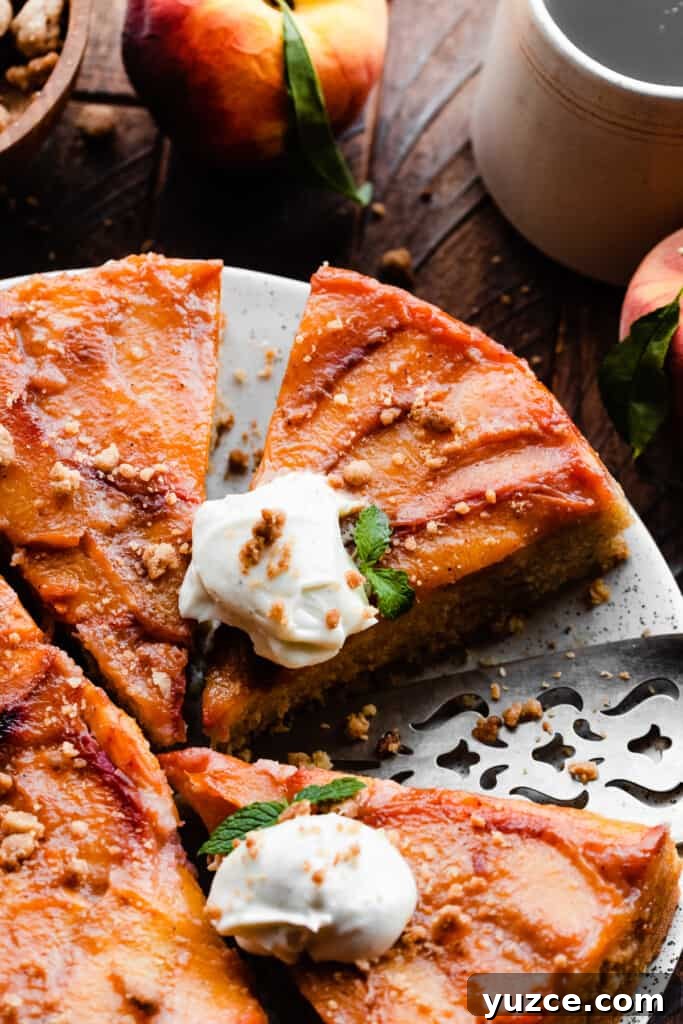 Slices of peach upside down cake on a plate, topped with whipped cream and streusel.