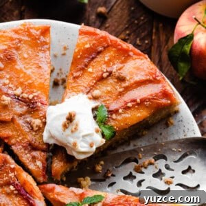 A close-up on slices of the peach upside down cake on a plate, topped with whipped cream.