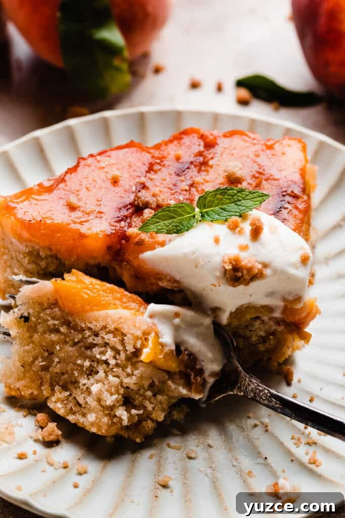 A close-up on a fork taking a bite out of peach upside down cake.
