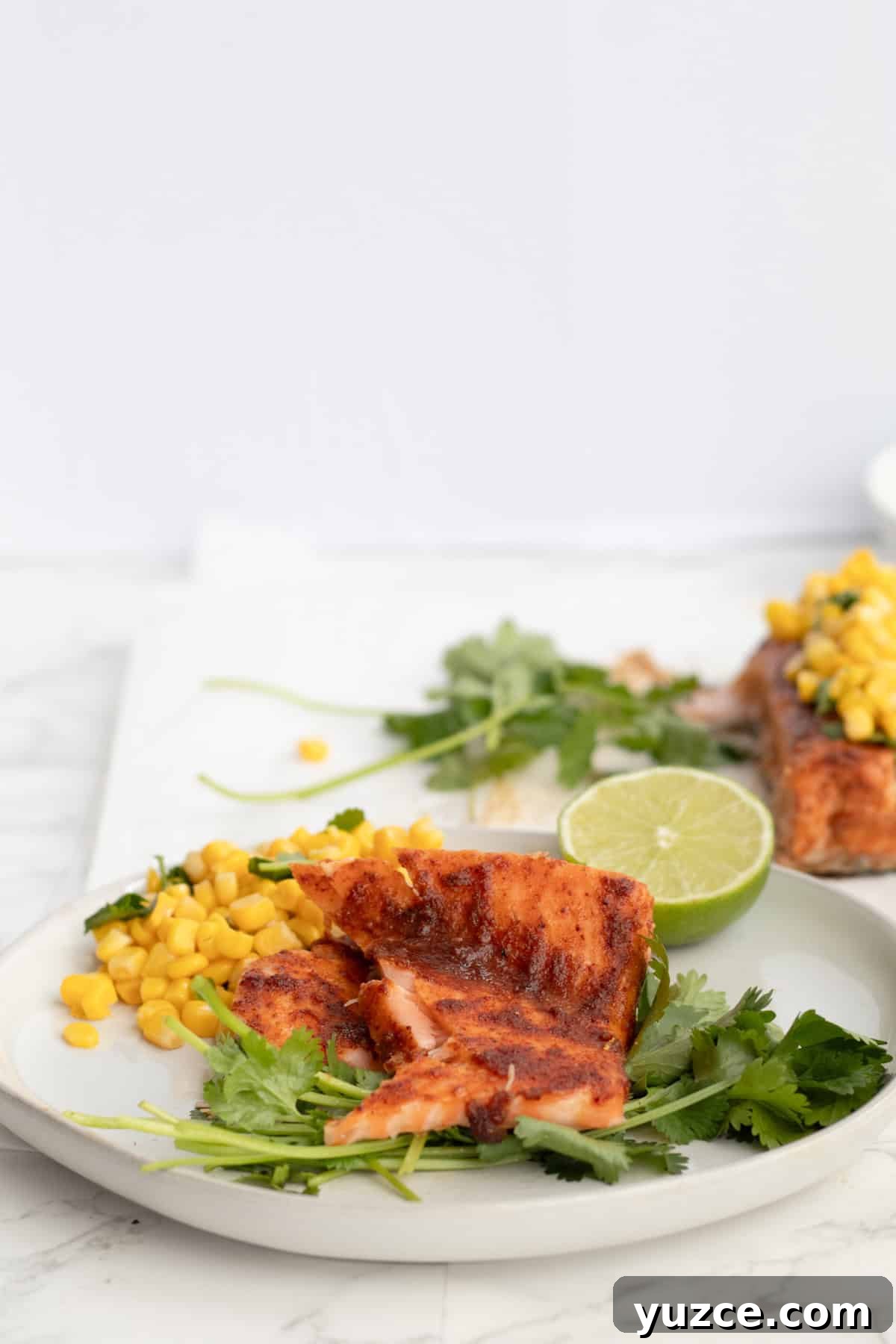 20-Minute Baked Chili-Lime Salmon Recipe 7 pieces of chili lime salmon on a white plate with corn and cilantro