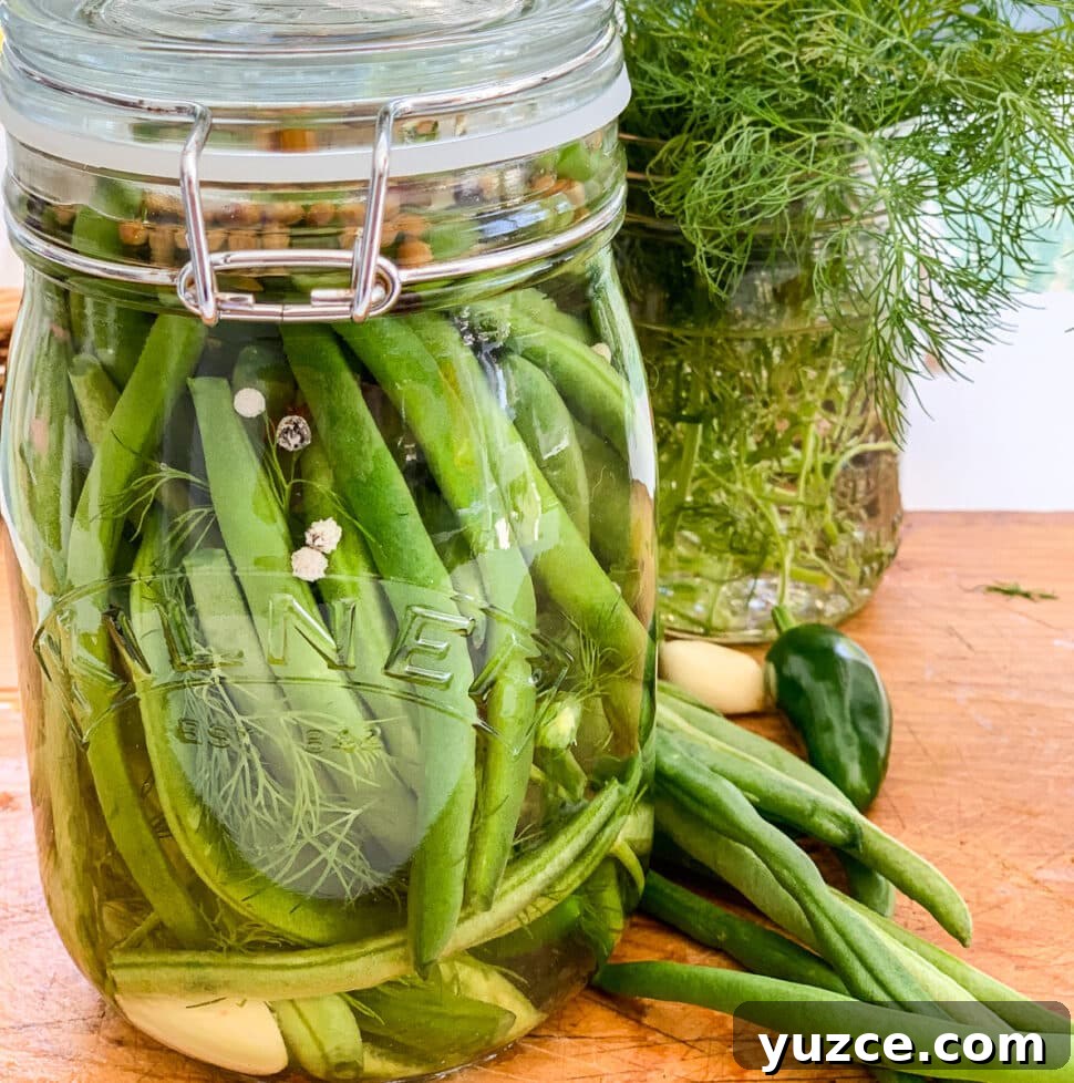 Dilly Pickled Green Beans Recipe: Classic Refrigerator Dilly Beans 19 A clear glass jar filled with pickled green beans on a cutting board.