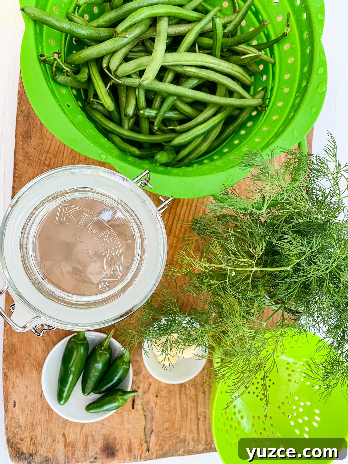 Dilly Pickled Green Beans Recipe: Classic Refrigerator Dilly Beans 7 A cutting board with a green colander filled with green beans and ingredients.