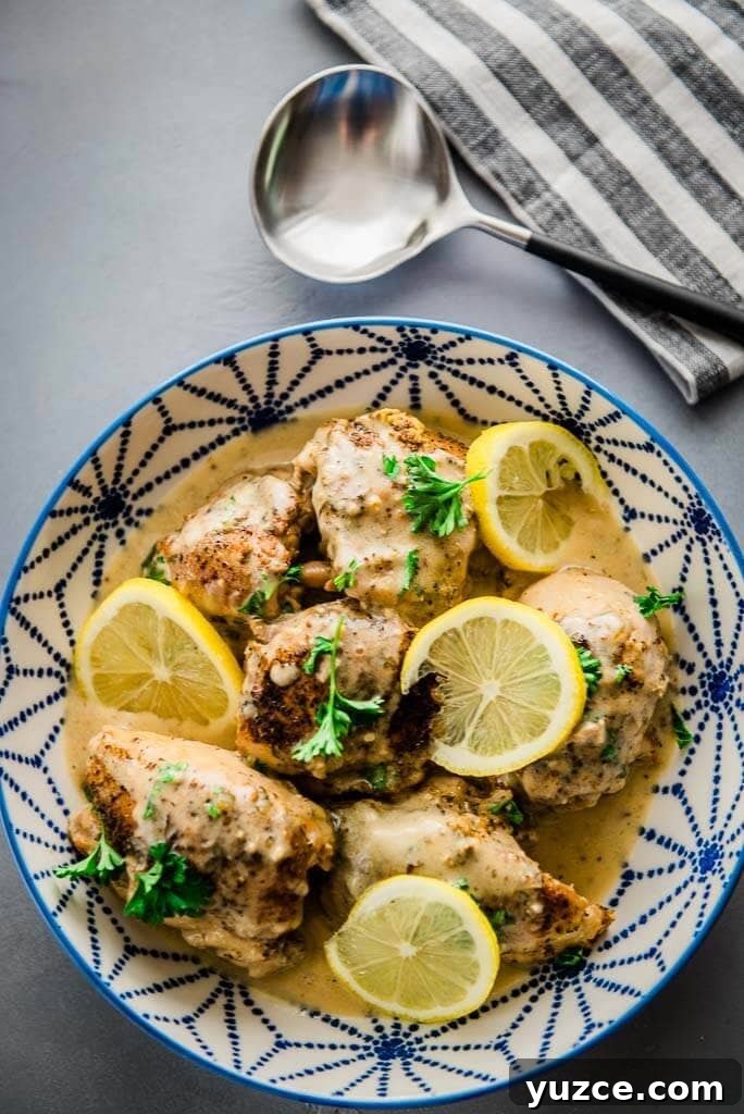 Lemon Garlic Instant Pot Chicken Thighs with Creamy Sauce 4 chicken thighs in a blue and white serving bowl topped with lemon slices