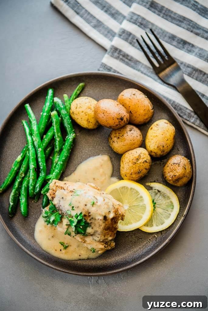Lemon Garlic Instant Pot Chicken Thighs with Creamy Sauce 5 chicken thighs with lemon sauce, lemon slices, green beans and baby potatoes on a gray plate