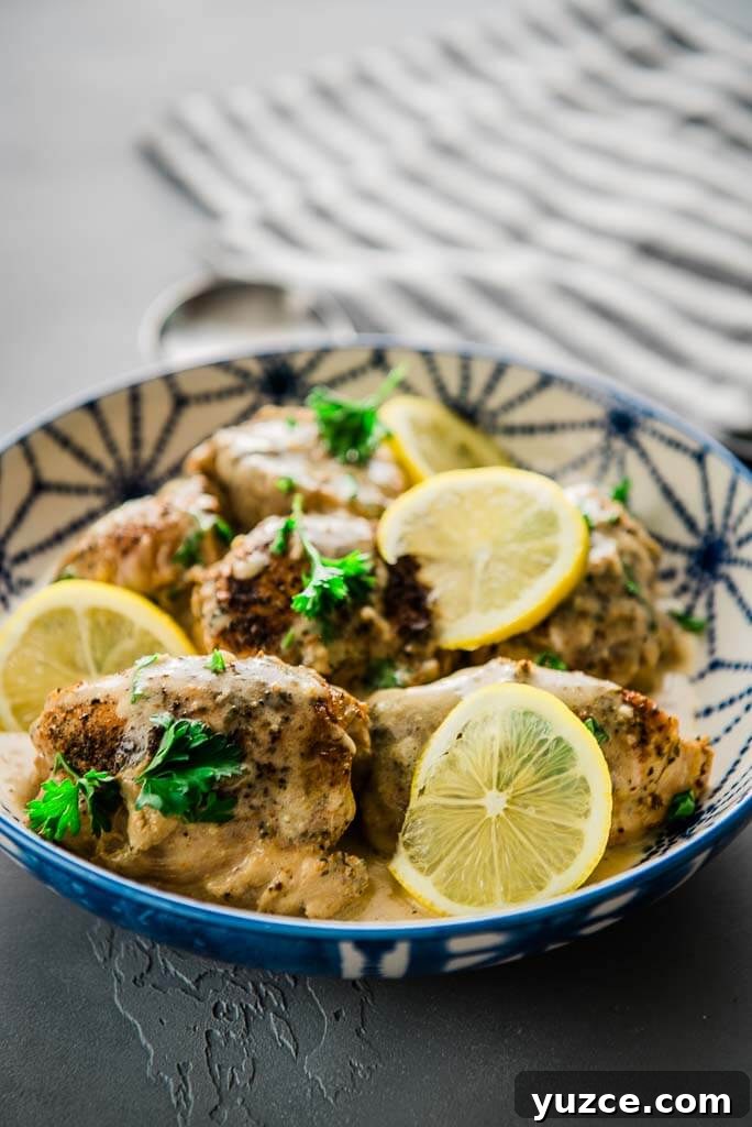 Lemon Garlic Instant Pot Chicken Thighs with Creamy Sauce 7 chicken thighs in a blue and white serving bowl topped with lemon slices