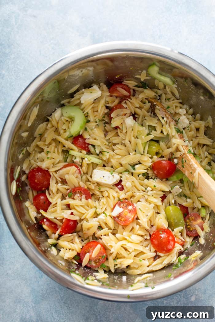 Greek Orzo Salad with Feta, Cucumber & Lemon Dressing 8 Wooden spoon stirring together greek orzo salad in a metal bowl