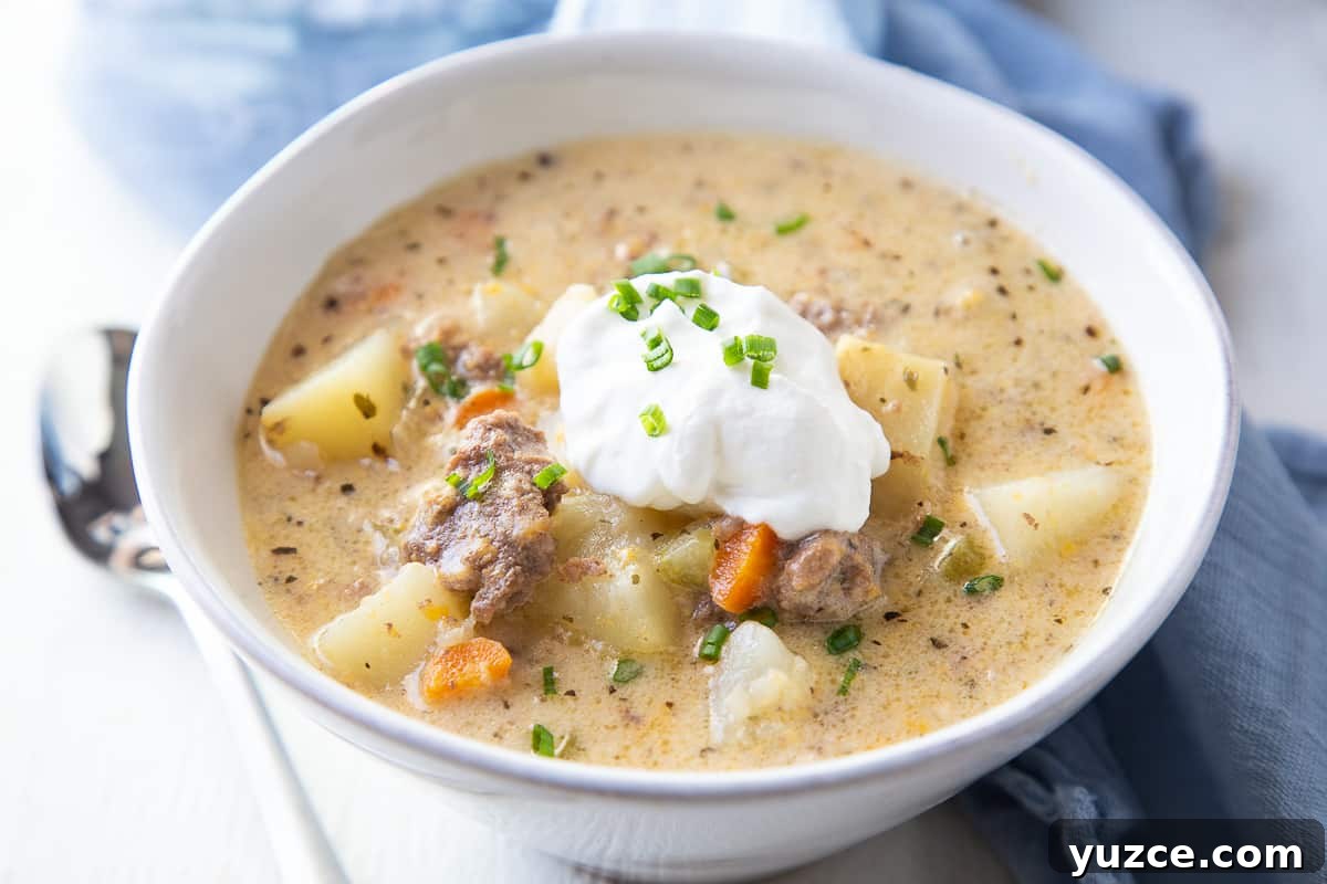 Slow Cooker Cheeseburger Soup Recipe for Comforting Weeknights 9 bowl of cheeseburger soup with sour cream and chives next to a spoon.