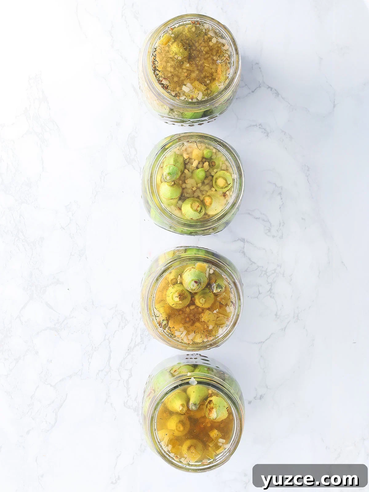 Tangy Spicy Pickled Okra Recipe for Bold Flavor 8 Four open jars of pickled okra lined up on a marble background.