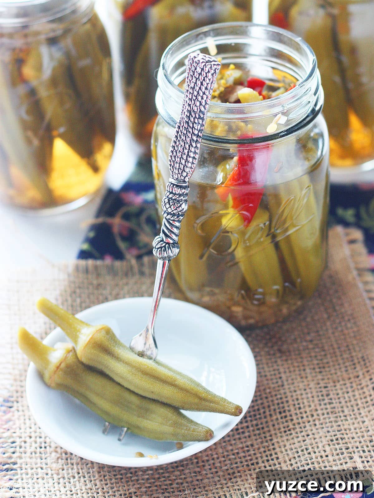 Tangy Spicy Pickled Okra Recipe for Bold Flavor 10 Sterling silver cocktail fork with two okra speared on the end leaning against an open jar of pickled okra.