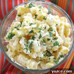 Mexican street corn in a glass cup topped with Cotija cheese and chopped cilantro on a colorful napkin.