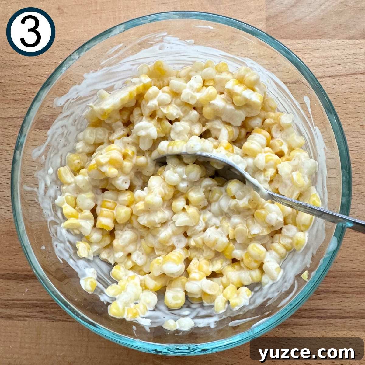 Corn kernels mixed with lime crema mixture in a glass bowl.