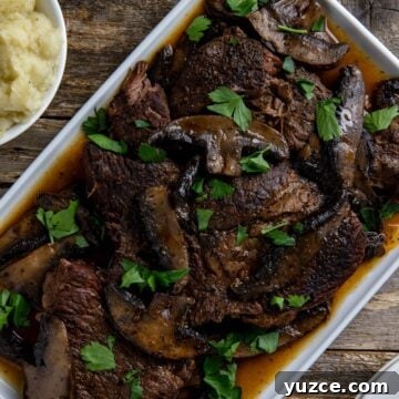 Cooked sliced roast topped with mushrooms and sliced portobella mushrooms on a white serving platter.