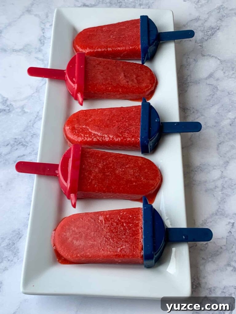 Five homemade strawberry popsicles on a white tray