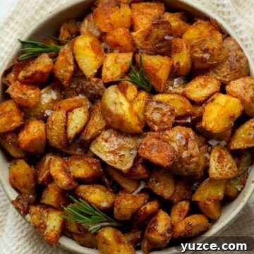 Extra cispy oven roasted potatoes with golden brown edges, garnished with fresh rosemary sprigs and flaky sea salt.