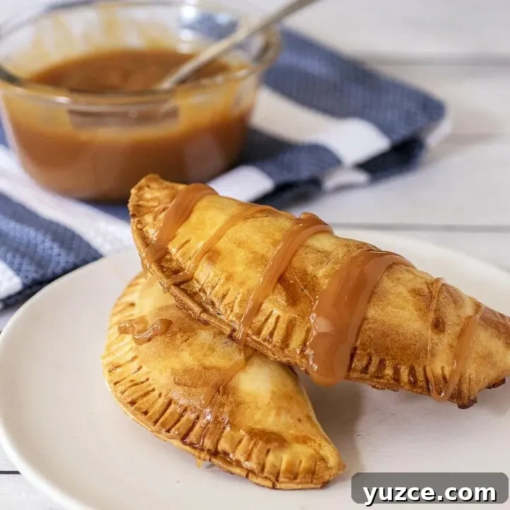 Two air fried empanadas on a plate in front of a dish of caramel sauce.