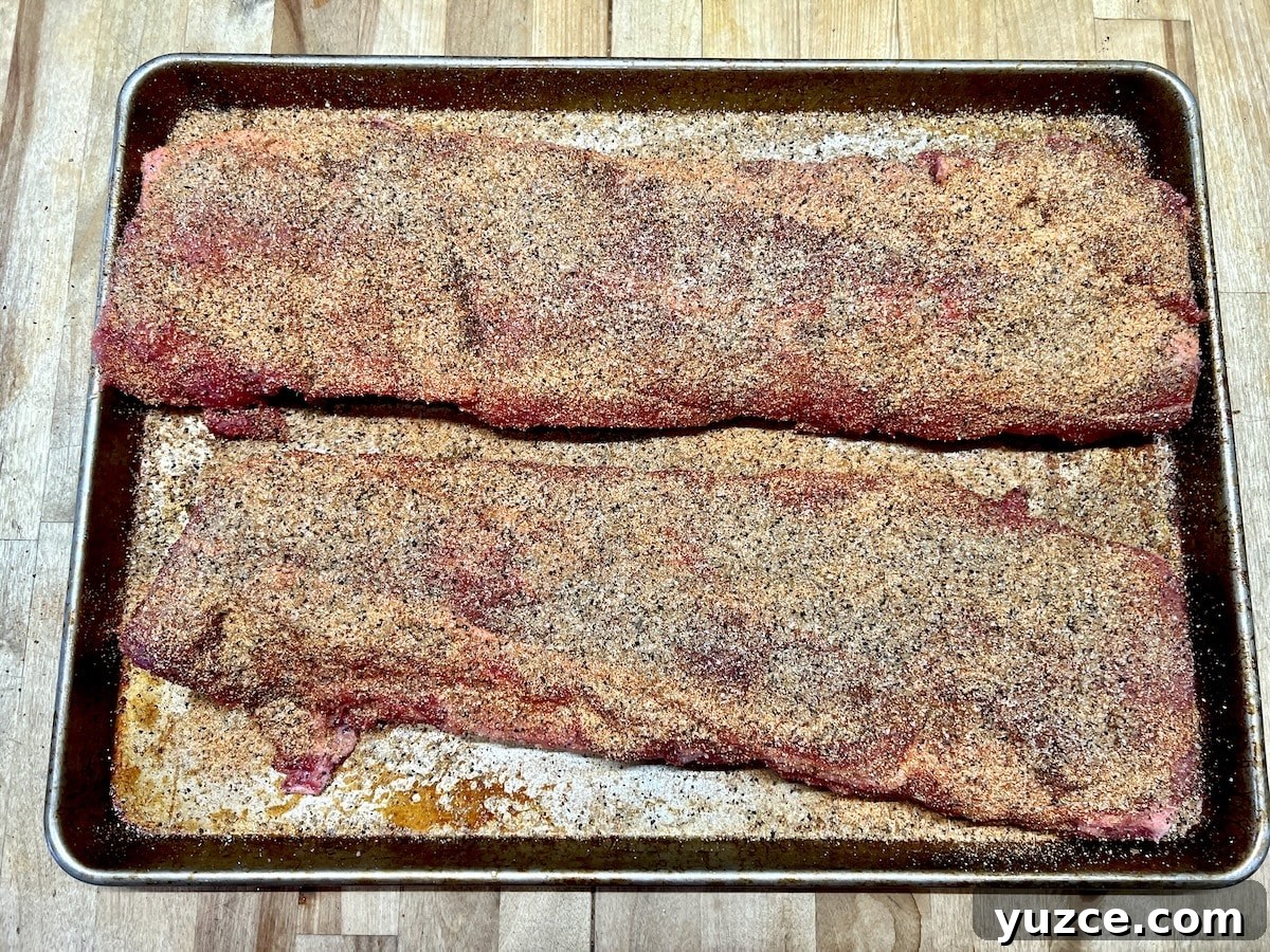 Grilled ribs with dry rub and spicy glaze. 2 racks of ribs with dry rub seasoning on a sheet pan.