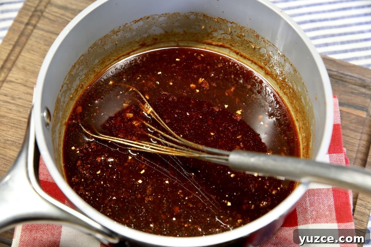 Spicy maple glaze for pork ribs. Pan of spicy maple glaze with a whisk.