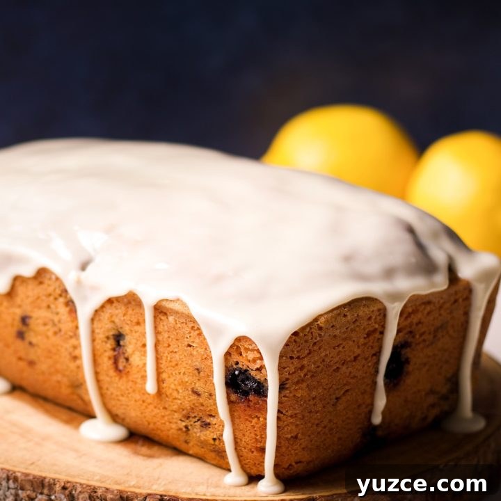 A blueberry loaf cake covered in lemon icing on a wood serving tray.