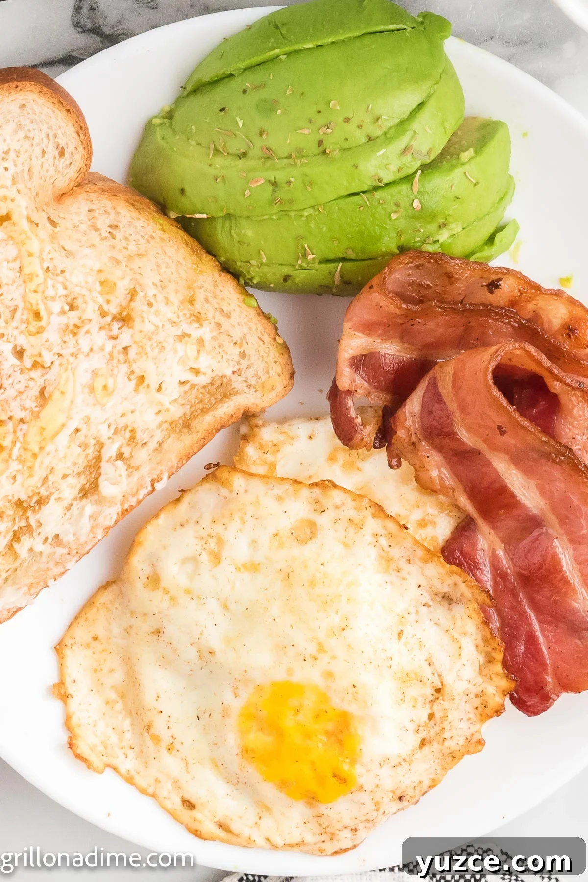How to Make Over-Hard Eggs on a Blackstone Griddle 2 Over Hard Eggs on a plate with bacon and toast and slice avocado