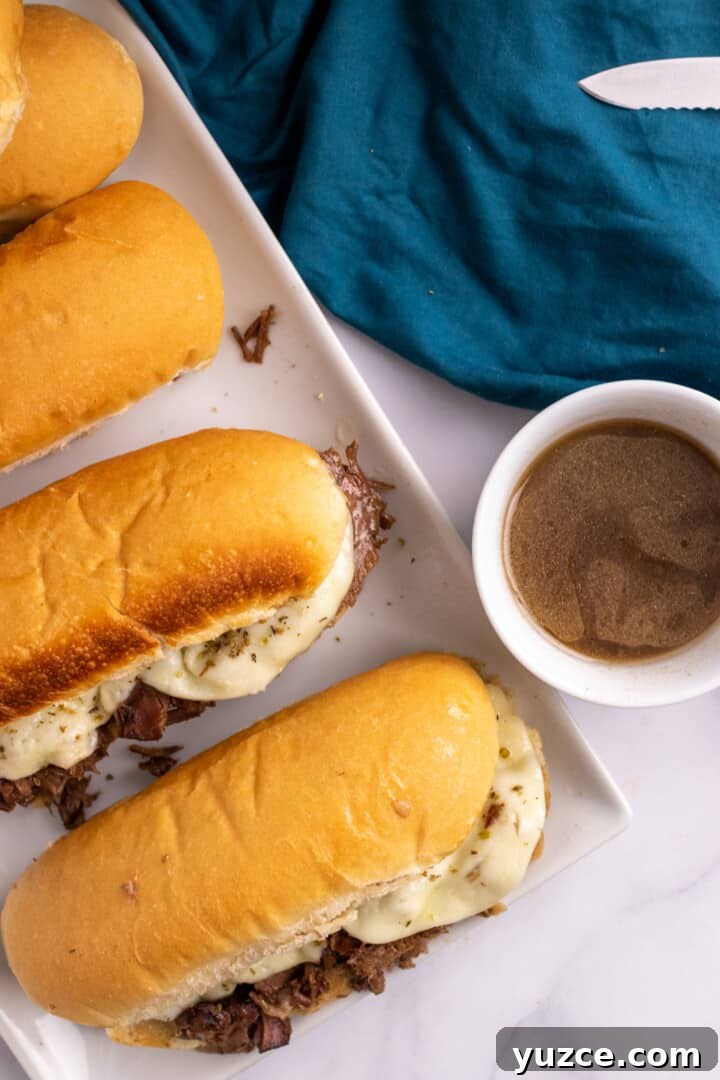 Slow-Cooker French Dip Sandwiches with Savory Au Jus 7 French Dip Sandwiches on white serving tray with au jus.