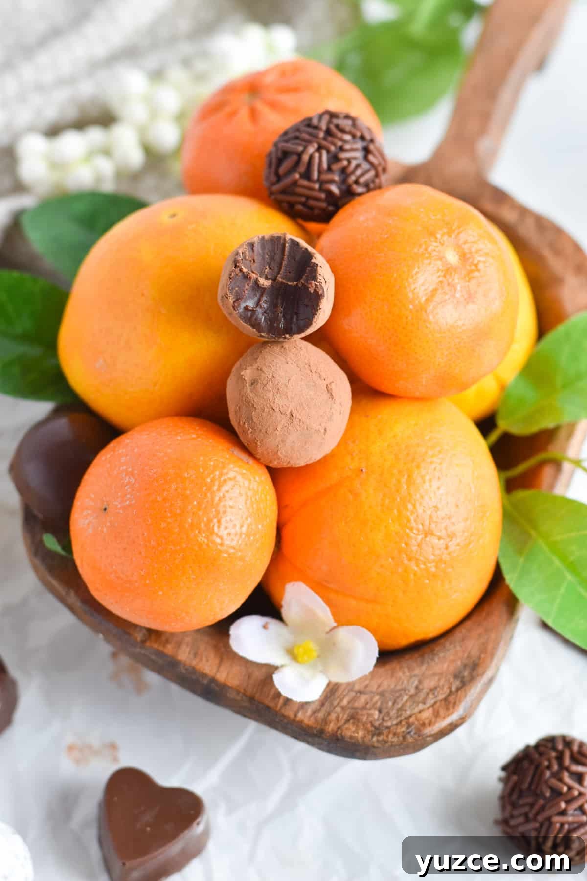 Decadent Chocolate Orange Truffle Recipe for Giftable Sweets 5 oranges in wooden bowl with chocolate orange truffles on top.